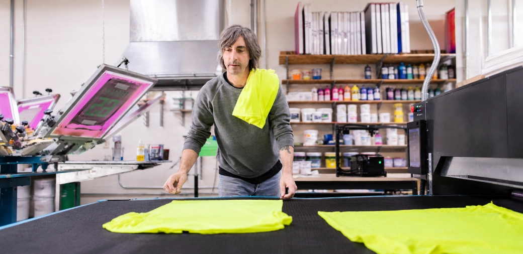 Printer laying out freshly printed t-shirts on the screen printing line